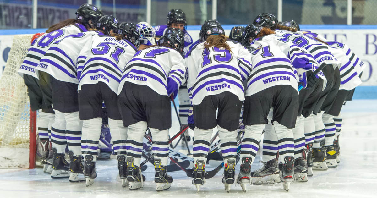 Western Mustangs women’s hockey team huddled in a circle in front of the net