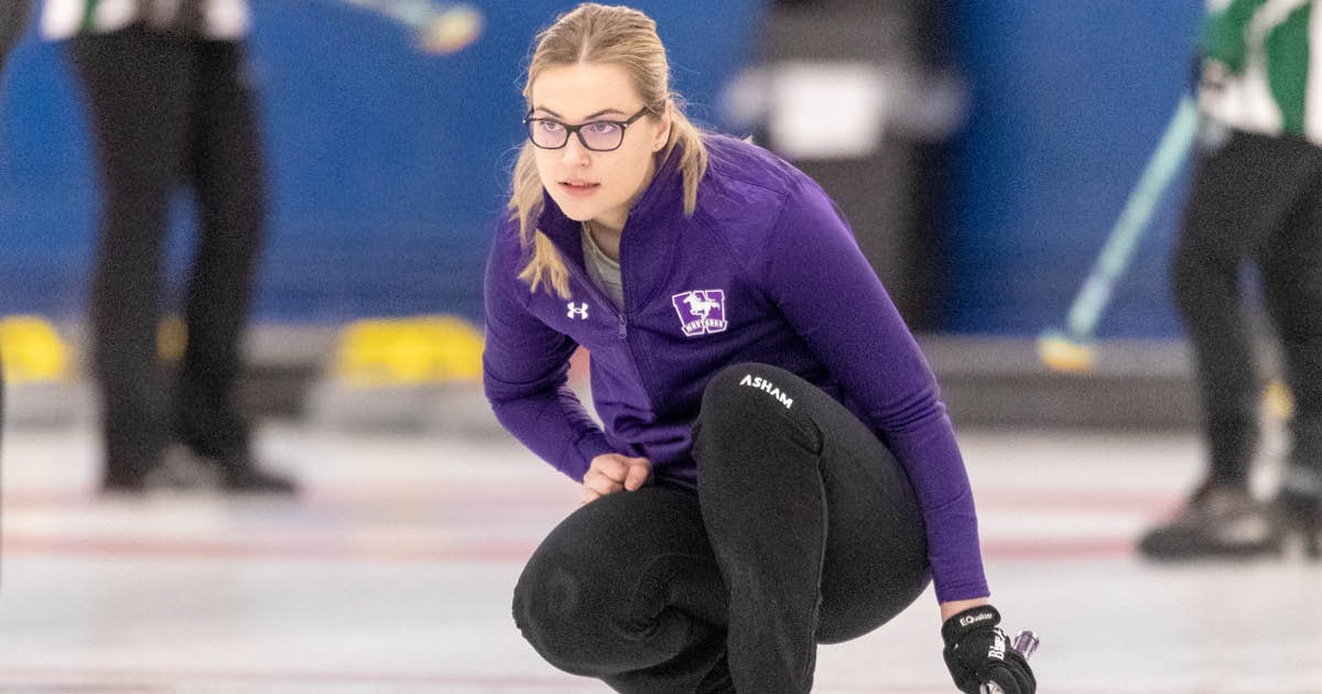 Western Mustangs women’s curler crouching and looking down the curling sheet