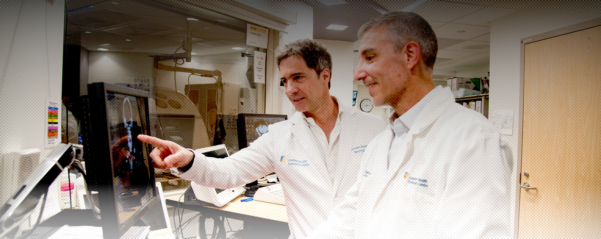 Two scientists in lab coats look at and discuss data on a computer screen in a laboratory setting